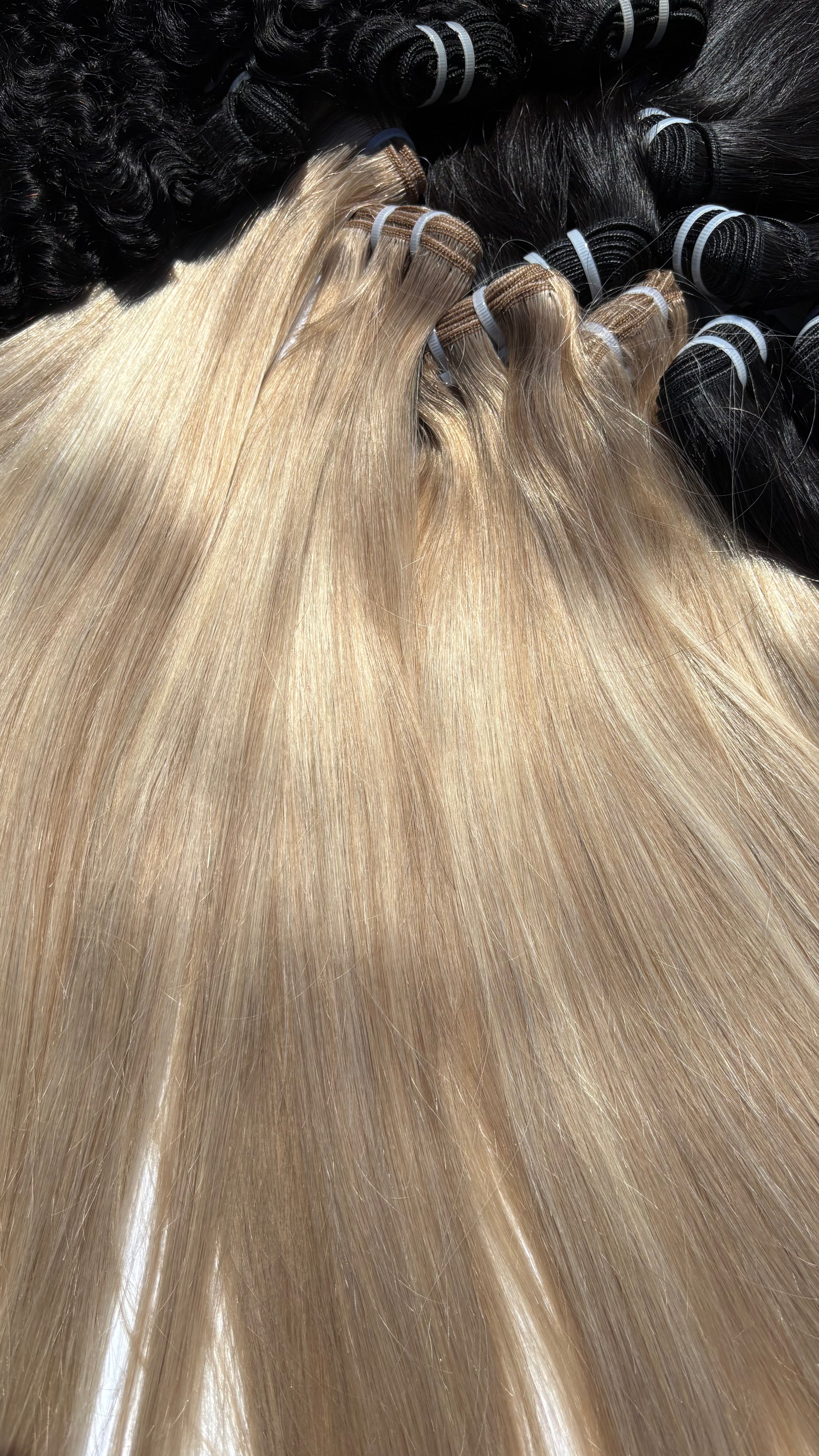 Long, straight blonde hair extensions laid out in bundles, with darker black hair bundles visible in the background.