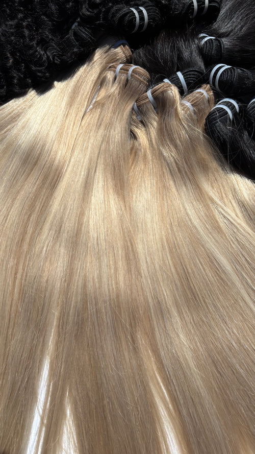 Long, straight blonde hair extensions laid out in bundles, with darker black hair bundles visible in the background.
